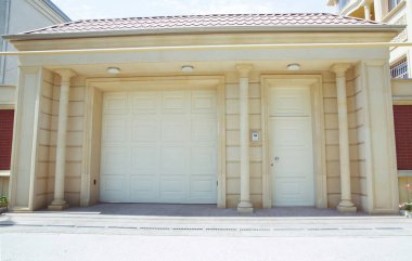 Otomatik elektrikli çekiş kapısı ya da modern binanın zemin katındaki şınav kapısı. Kapalı kapı ya da patenli kapı ve beton zemin. Beyaz otomatik panjurlar. Garajdaki kapılar