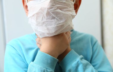 Corona virüsüne karşı koruma. Hastalıklı bir çocuk elini boğazına sürüklüyor. Yüzünde koruyucu maske takmış çocuklar öksürüyor, el ele tutuşuyorlar, boğazı beyaz duvarda ağrıyor.