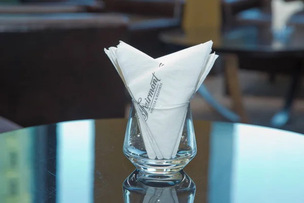 Θαμπάδα εικόνας-λευκή χαρτοπετσέτα τοποθετείται σε ένα ποτήρι στο τραπέζι στην αίθουσα δεξιώσεων. Τραπέζι φαγητού με διακοσμητική χαρτοπετσέτα, γυάλινα επιτραπέζια σκεύη στην τραπεζαρία του ξενοδοχείου . — Φωτογραφία Αρχείου