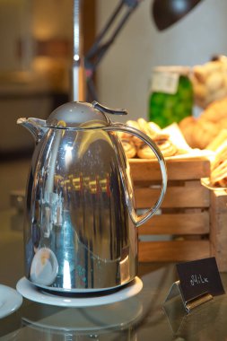 Lüks beş yıldızlı otelin ahşap masasında öğleden sonra sütü için sıcak su bulunan termos. Sıcak içecekler servis ediliyor. Kahve için metal süt kapağı.