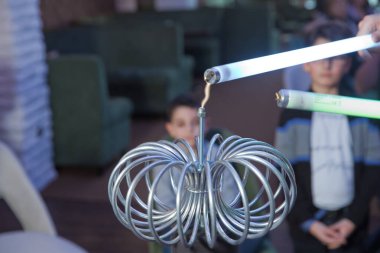 Elinde bir lamba tutuyor ve elektrostatik boşalımı izliyor. Bu yapay olarak havadaki elektriksel boşalımla meydana geliyor. Kablosuz elektrik Tesla Bobininin nasıl çalıştığını gösteriyor.