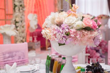Düğün günü masada güzel pembe ve beyaz çiçekler. Düğün masası, düğün süslemeleri. Güzel güllerle dolu büyük vazo yemek masasının üzerinde duruyor. Misafirler için düğün çiçeği kompozisyonu.