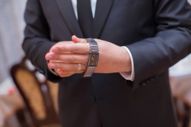 Adam saatlerce el ele tutuşuyor. Erkek işadamı giyinir ve saatini ayarlar. Toplantıya hazırlanır. Adam saati hazırlıyor.