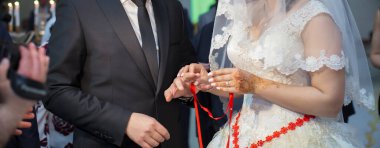 Damadın elini yakın çekimde gelinin parmağına alyans tak. Sol el. Gelin, bir erkeğin elinde yüzük takıyor.