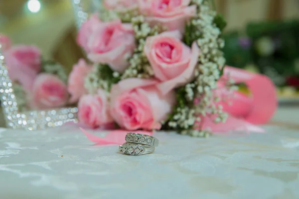 ピンクの結婚式の花 婚約指輪付きの花嫁と新郎がテーブルの上に置かれ 彼らの隣に結婚式の花束があります 白いテーブル 花束の選択的なフォーカスの横に結婚指輪 — ストック写真