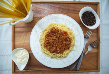 Lezzetli spagetti ahşap tepsisi. Kıymalı spagetti bolonez, soğan, doğranmış domates, domates püresi. Bir kasenin içinde çiğ makarna. Karabiber, kasenin içinde mayonez. Çatallar