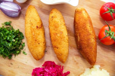 Maydanoz yapraklı tavuk pirzolası. Tahta üzerinde Ukrayna geleneği yemekleri. Küçük bir kasede kırmızı lahana turşusu. Patates püresi. Mayonez, sarımsak, soğan, domates. Doğranmış kişniş.