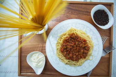 Lezzetli spagetti ahşap tepsisi. Kıymalı spagetti bolonez, soğan, doğranmış domates, domates püresi. Bir kasenin içinde çiğ makarna. Karabiber, kasenin içinde mayonez. Çatallar