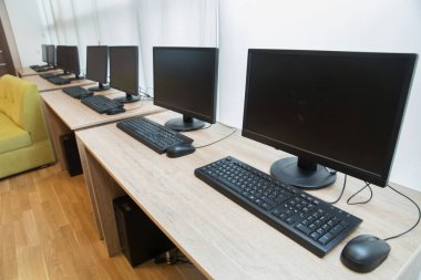 Bilgisayarlar masasında siyah ekranlı monitörler. Bir sürü bilgisayar ve masa. Klavye ve fare