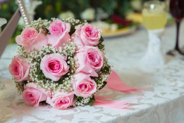 Pembe nişan buketi. Pembe kurdele. Beyaz masada pembe nişan çiçekleri. Nişan yüzüklü gelin ve damat pembe düğün buketini taktı.