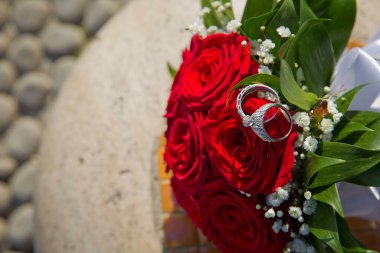 Gelin ve damat kırmızı bir düğün buketinde yüzükler takıyor. Düğün için bir buket gül..