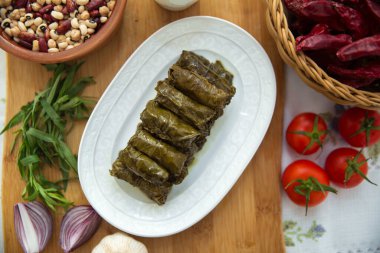Geleneksel Sepette Kırmızı Kuru Biber. Lezzetli dolma sarma pilavı, beyaz yoğurt sosu. Sarımsak, kırmızı soğan, tarhun otu. Doldurulmuş beyaz bir tabakta. Kahverengi bir kasede yoğurt ve kuru fasulye. Domatesler