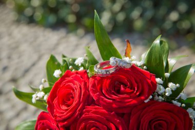 Gelin ve damat kırmızı bir düğün buketinde yüzükler takıyor. Düğün için bir buket gül..