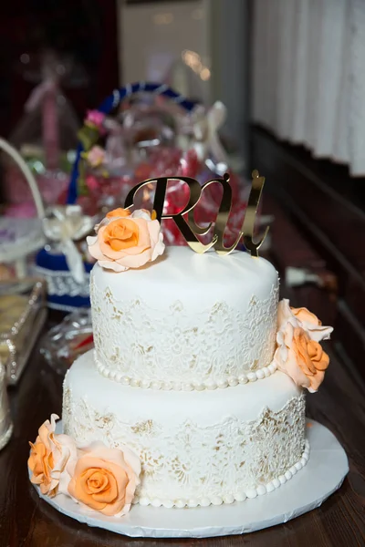 White Two-tiered cake . There are yellow flowers on the cake. The letter U and R are written in gold on the cake.