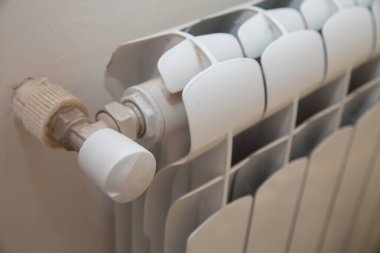 Ev ısıtıcısının düzenleyicisi. Evdeki ısıtıcıyı kapat, hidrolik ekipman. Isıtıcı. Evdeki pencerenin altında termostatı olan beyaz bir radyatör. Evde ısıtıcı var. Beyaz.