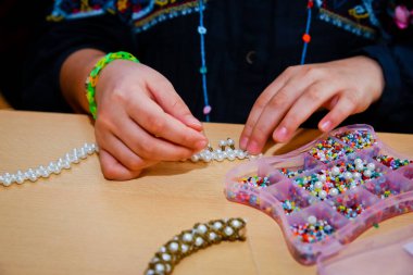 Çocuk boncukları eline koyuyor. Ufacık delikli boncuklar.