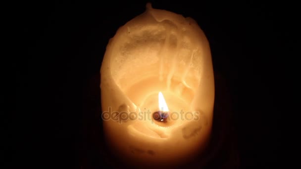 Uma chama em uma vela de cera branca com cera pingando em um quarto escuro . — Vídeo de Stock