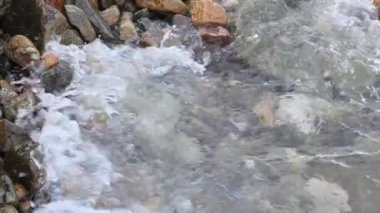 Küçük çakıl taşları ve deniz sörf ile çakıl plajı. Kayalık sahil çalıştırmak günbatımı, dalgalar.