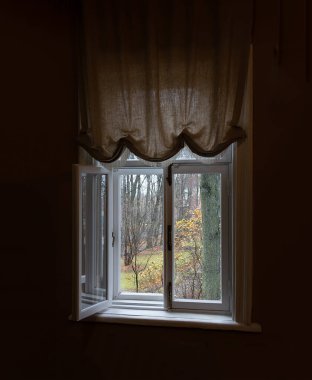 Sonbahar ormanına bakan karanlık bir odada açık bir pencere.