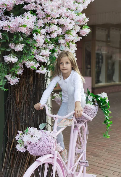 Kleines Mädchen auf rosa Fahrrad. mit einem Korb voller Blumen — Stockfoto