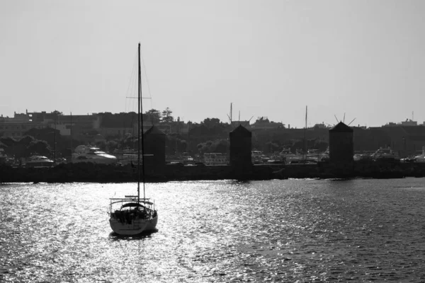 Black and white silhouette of a yacht entering the port of Rhodes at sunset — Stock Photo, Image