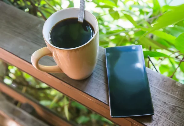 Black coffee in cup and smartphone outdoors — Stock Photo, Image