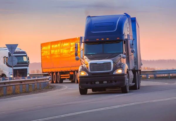Вантажівки їдуть по шосе на заході сонця — стокове фото