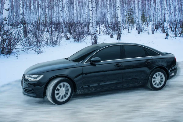 Black car moves in winter on a snowy road — Stock Photo, Image