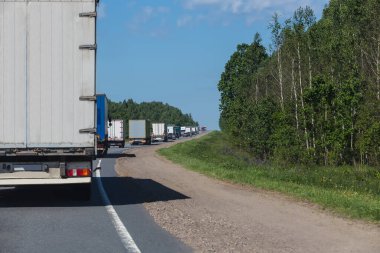 Banliyö otoyolu boyunca giden uzun bir kamyon konvoyu.