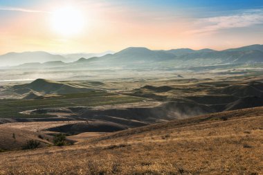 Vadilerle, vadilerle, parlak güneşli gökyüzünün altındaki dağlarla dolu bir manzara.