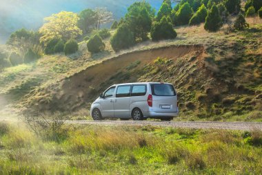 Minivan yazın güneşin aydınlattığı bir dağ yolunda hareket eder.