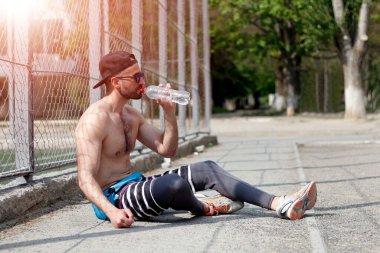 Açık havada yapılan egzersizden sonra su içen genç bir adam.