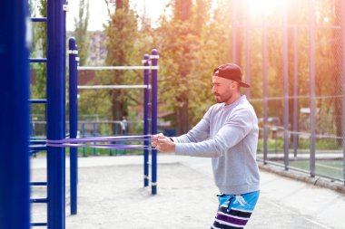 Güçlü genç adam spor parkında lastikle sıkı egzersizler yapıyor.