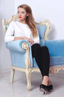 Bir kız bir beyaz kazaklı bir kırmızı koltukta oturuyor