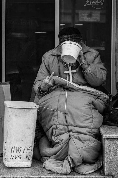 Бездомный сидит на улице.
 