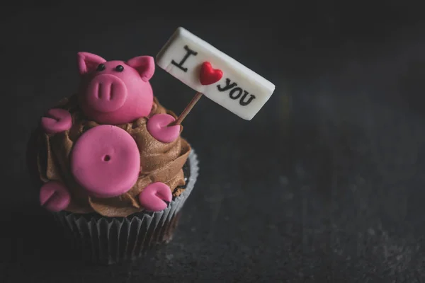 Cup cake with pig holding I love you sign on the dark background with blank space,selective focus and valentines day concept