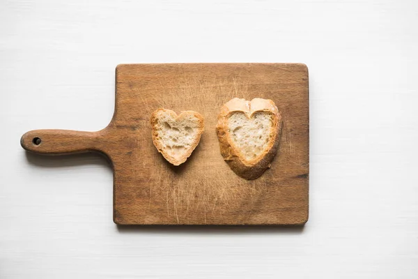 Heart-shaped slices of bread on old cutting board love concept — Stock Photo, Image