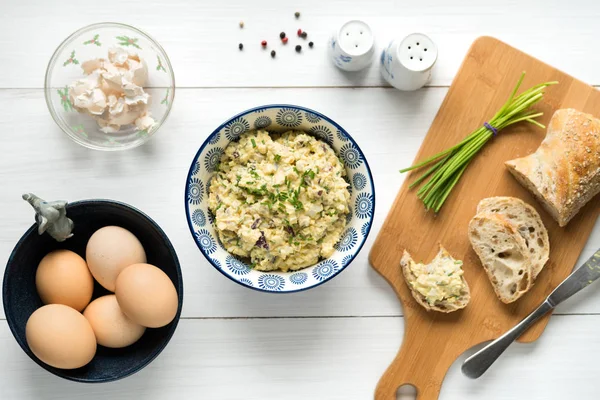 Ensalada de huevo en un bol cubierto con cebollino arreglado en una mesa blanca fro — Foto de Stock