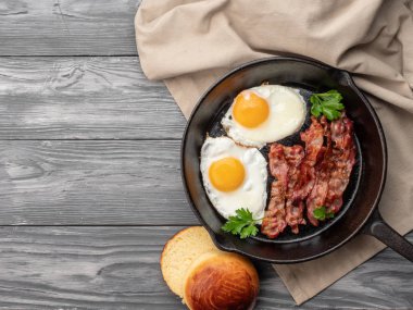 Domuz pastırmalı sahanda yumurta ve ahşap bir yüzeyde çörek. Üst Manzara. C