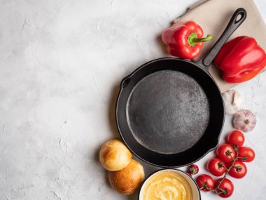 Beton yüzeyde boş bir tava, üst manzara. Çevrede çeşitli sebzeler.