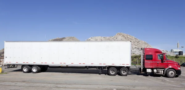 Trucking industry: side view of parked red semi cab and white trailer against blue sky.
