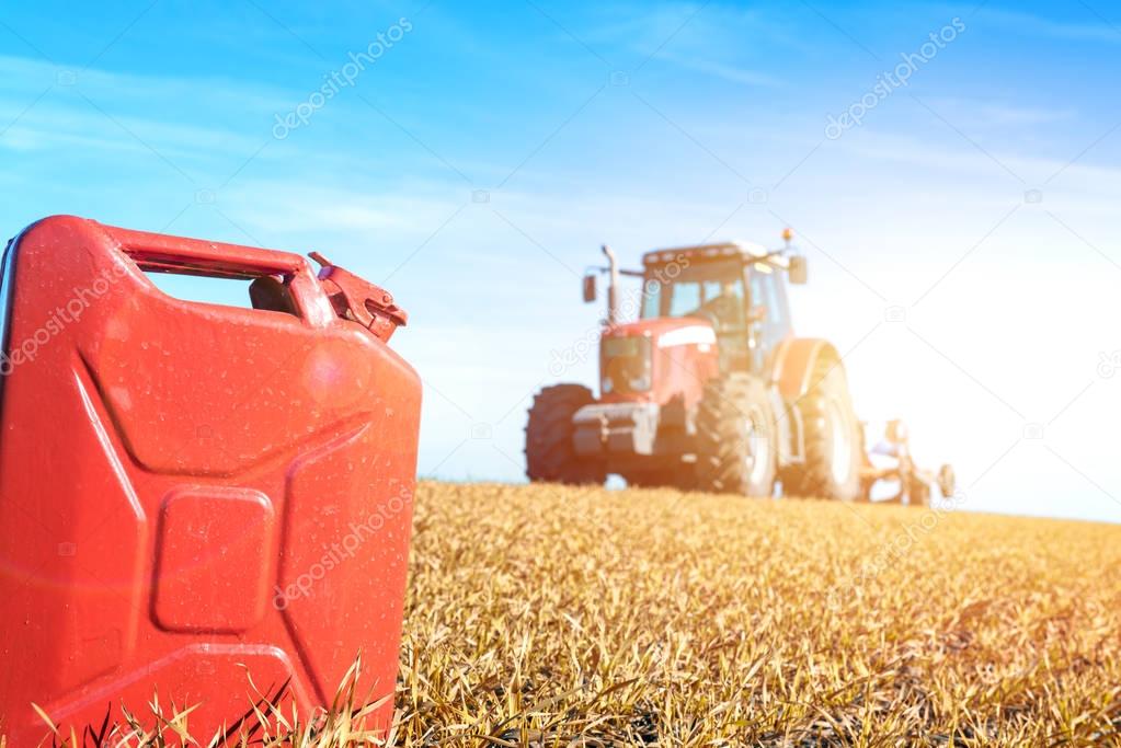 Tractor cultivating in the field with gas can petrol, diesel, bio fuel. Agriculture and farming.