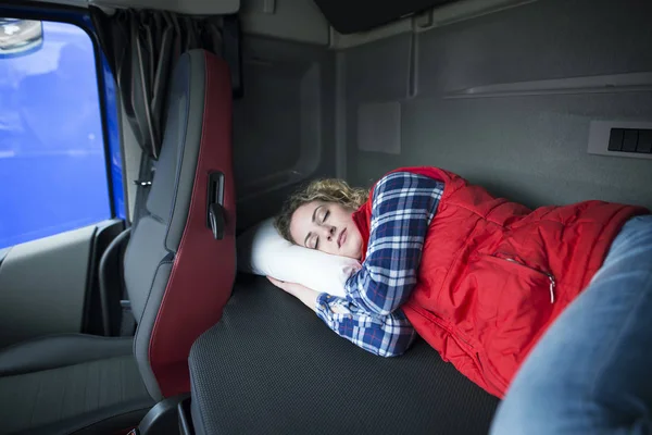 Shot of tired truck driver sleeping in cabin of his truck due to driving long distances and overworking. Trucker lifestyle.