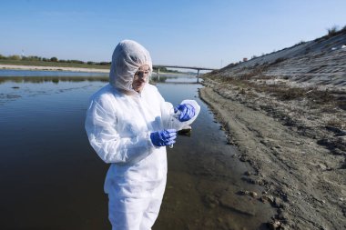 Female ecologist expert in protective clothes examining water quality and purity. Save the environment.