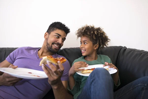 Father and daughter enjoying pizza in comfortable living room sofa.