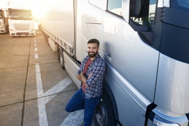 Middle aged professional trucker with crossed arms standing by his truck. Transportation services.