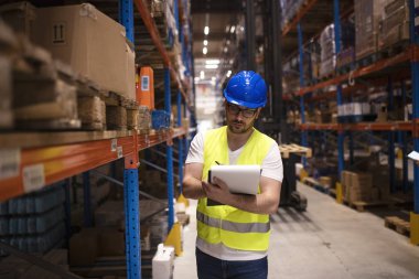 Warehouse worker writing down inventory report on products in large storage area. Working in warehouse department.