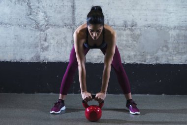 Fitness woman in sports clothes exercising with kettle bell weight in the gym. Training and sport.