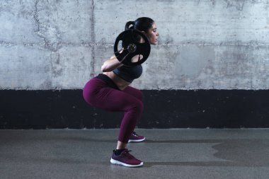 Sporty fitness woman in crouching position doing squats and lifting weight in the gym.