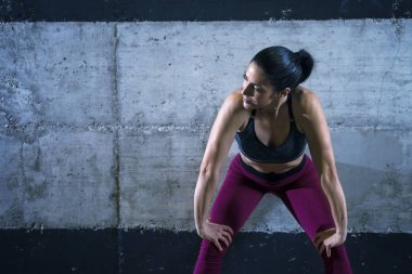 Training and sport. Fitness woman in sports clothes leaning on concrete background and looking aside. Copy space.
